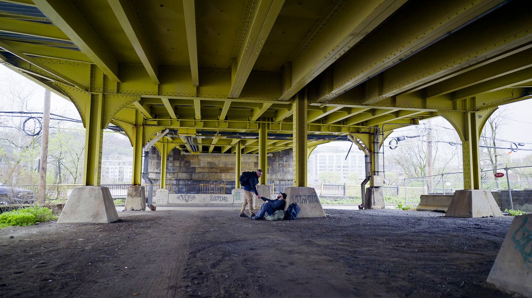 A Semper Fi Mission volunteer reaching out to help a man experiencing homelessness under a bridge